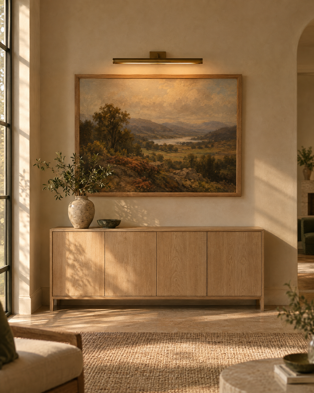 Brass picture light illuminating a landscape painting above a sideboard